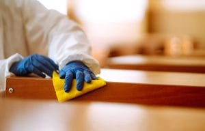 Worker in protective suit cleaning a wood surface with a yellow microfiber