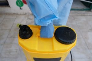 Biohazard worker carrying a large yellow canister with cleaning agent