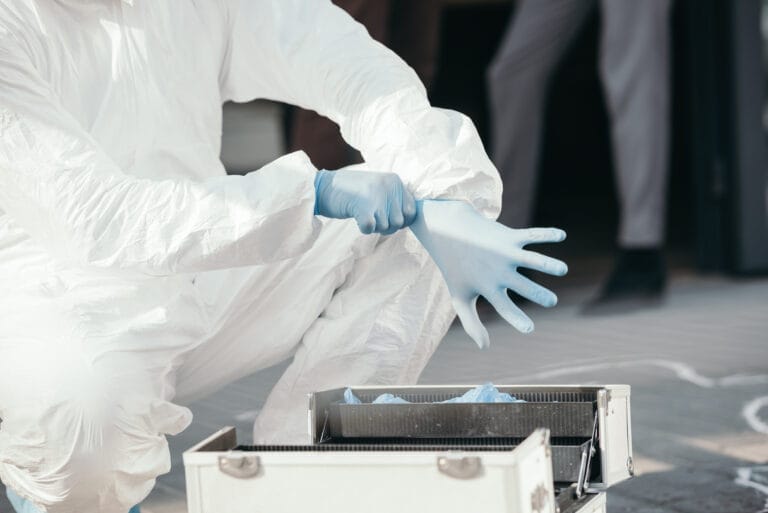 Criminologist in latex gloves examines evidence, highlighting biohazard cleanup services in California’s Monterey Bay Area.
