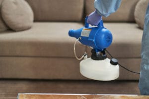 restoration experts Boise ID - Male hands in protective gloves using a microparticle gun for virus prevention near a sofa, re