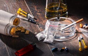 meth testing - Various addictive substances like alcohol bottles, cigarette packs, and drug paraphernalia on a table, relatin